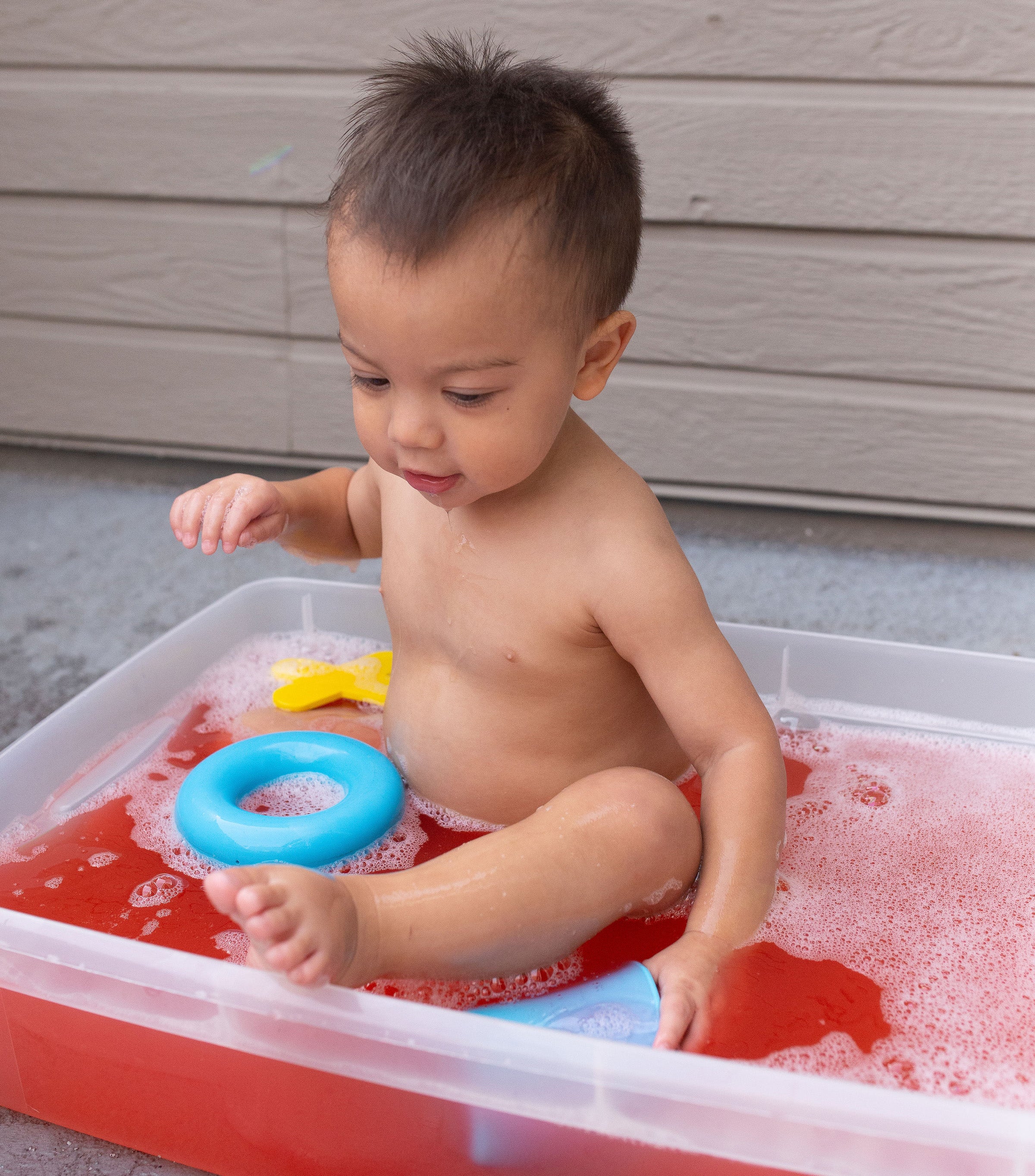 Child playing with water and toys in a portable bathtub outdoors.
