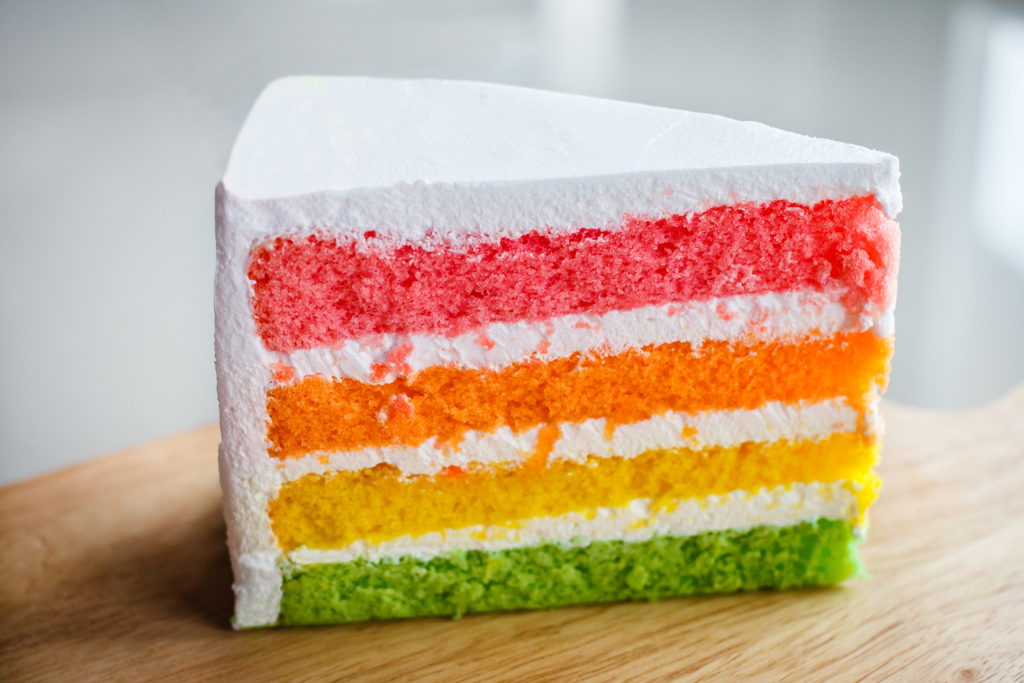 Colorful layered cake slice on a wooden board with a blurred background
