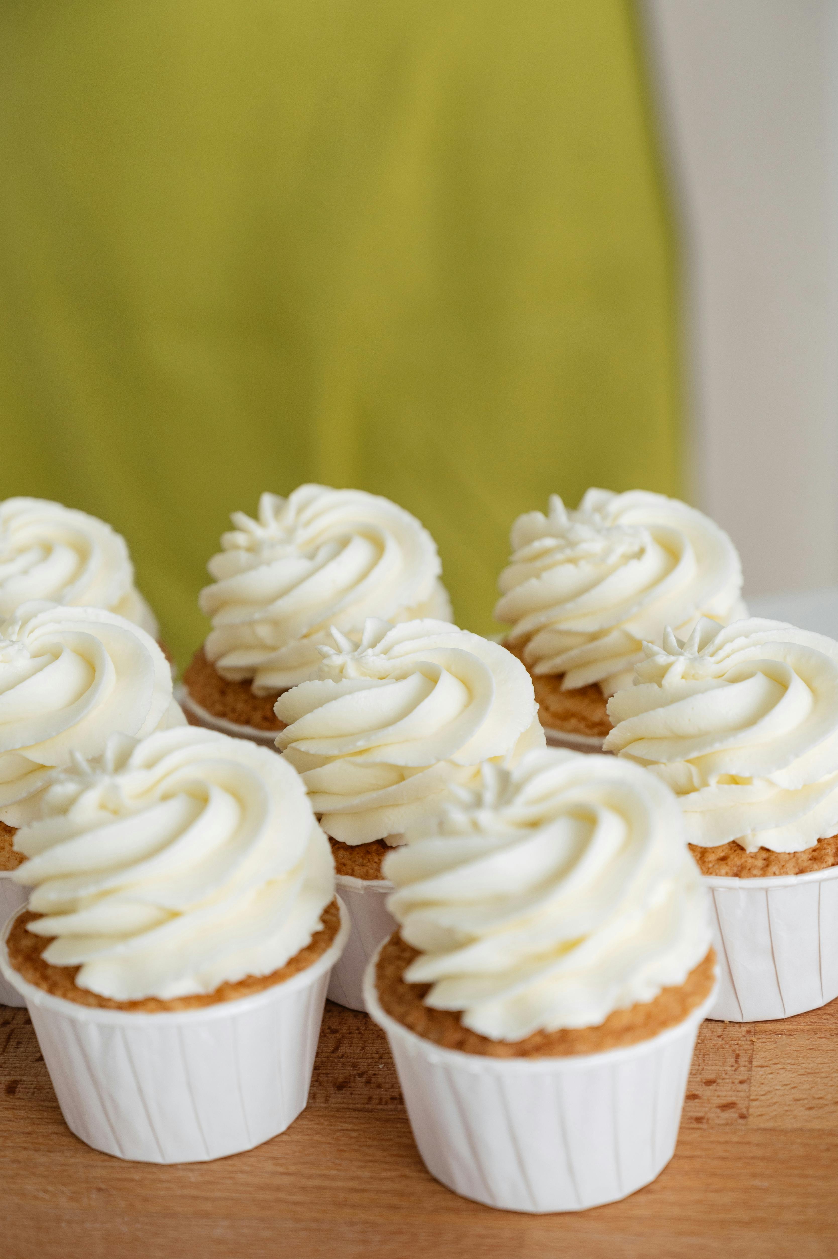 Cupcakes with white frosting on a wooden surface with a green curtain in the background